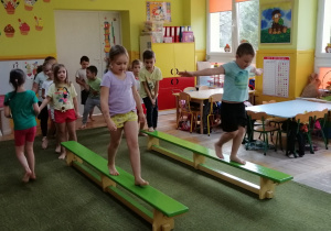 Dzieci ćwiczą równowagę, przechodząc po ławeczce